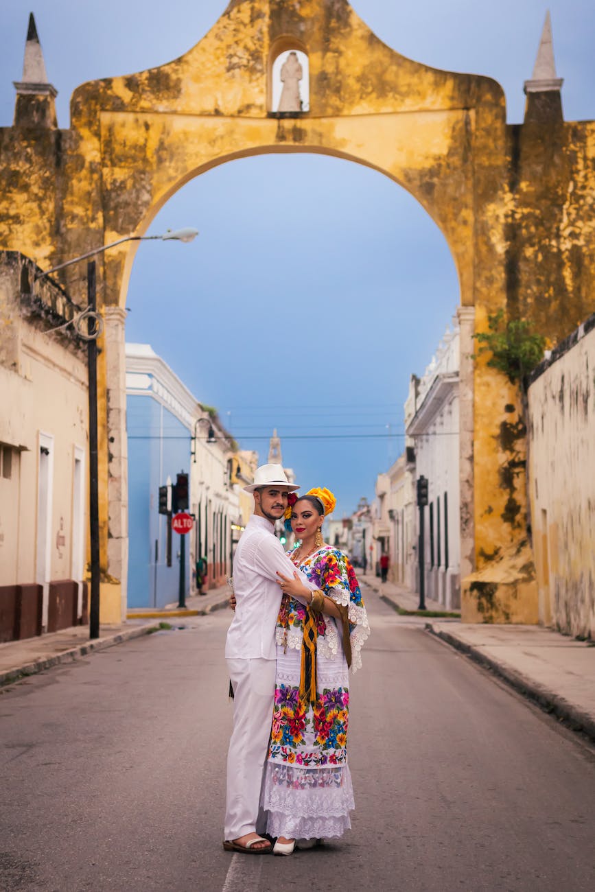 couple wearing traditional clothing hugging in front of the merida arch uxmal mexico